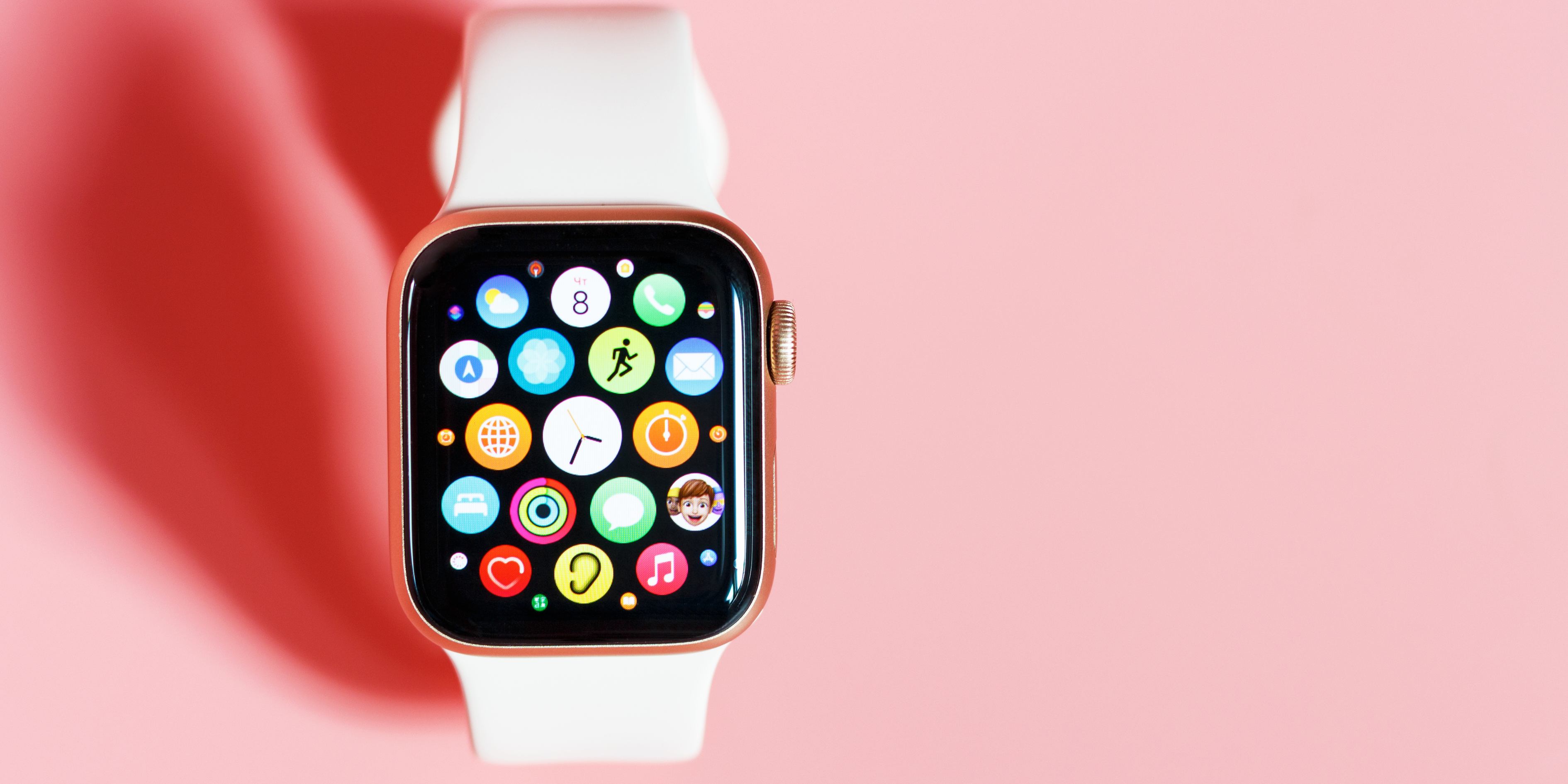 Apple Watch with colorful app icons on display, white band, placed against a pink background

